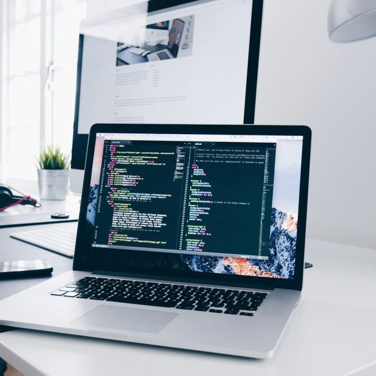 Softwareentwicklung Laptop mit Codezeilen auf dem Bildschirm, daneben Smartphone und Pflanze auf einem Tisch.